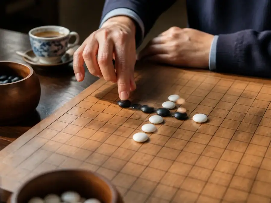 A player placing a critical Gomoku stone at a tea table